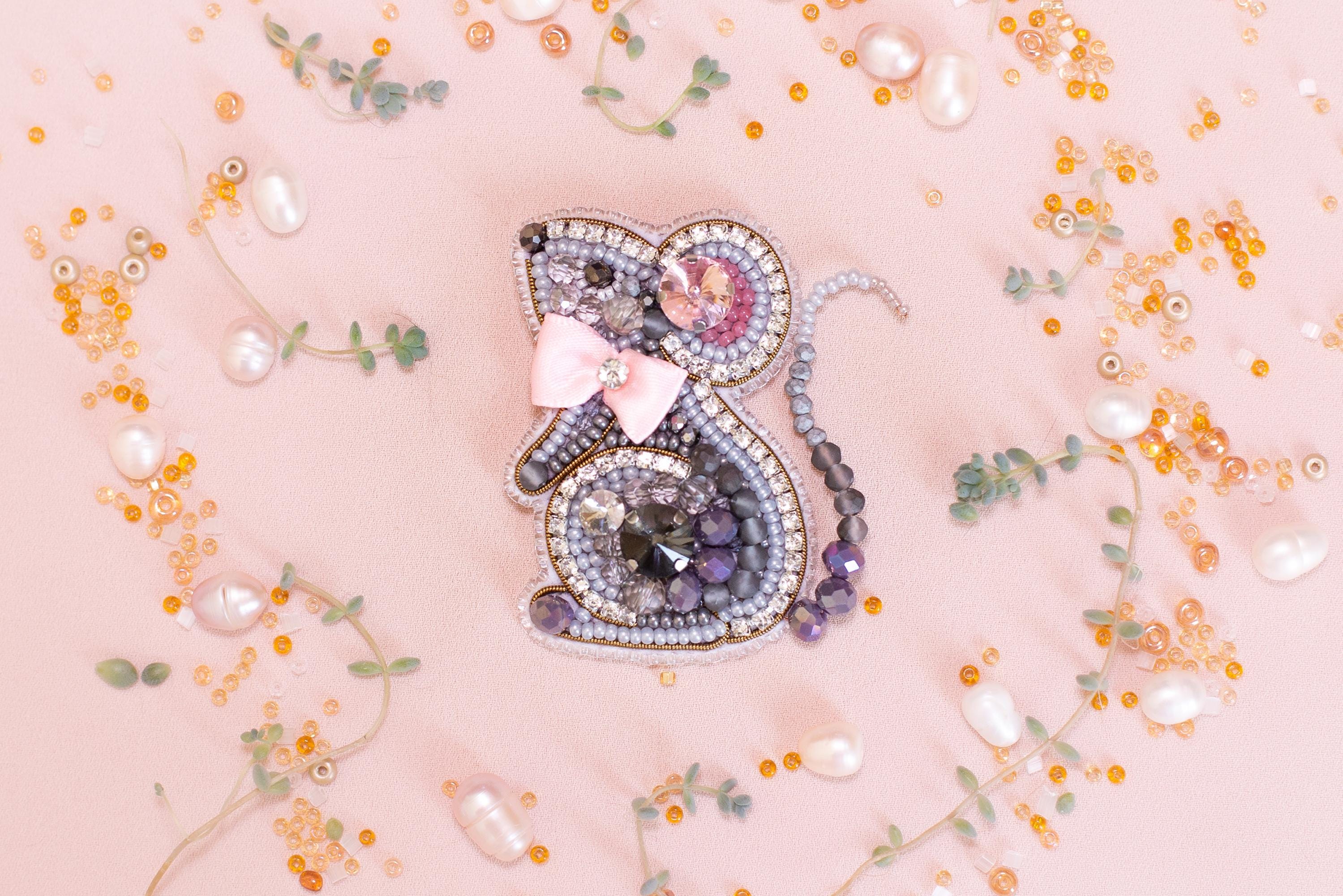 a decorative piece of jewelry, possibly a brooch or pendant, surrounded by various beads, pearls, and flowers in shades of pink, purple, and orange.